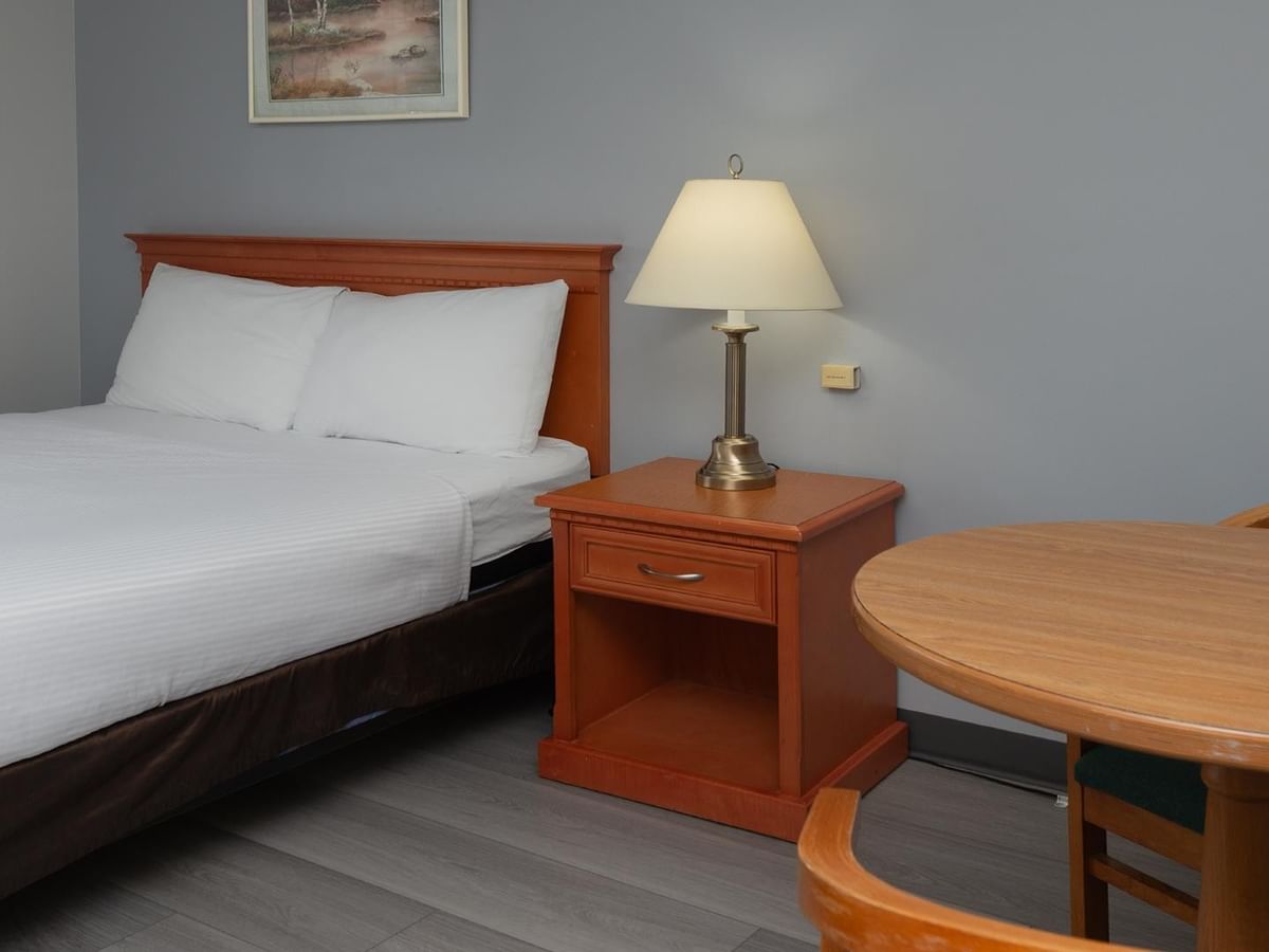 Coast Queen Pet Friendly room with queen bed, wooden nightstand, table lamp, and round dining table.