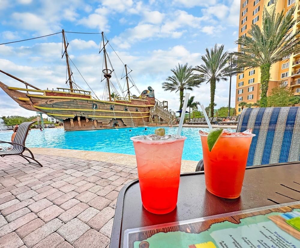Two tropical drinks by pool with pirate ship and building at Lake Buena Vista Resort Village & Spa