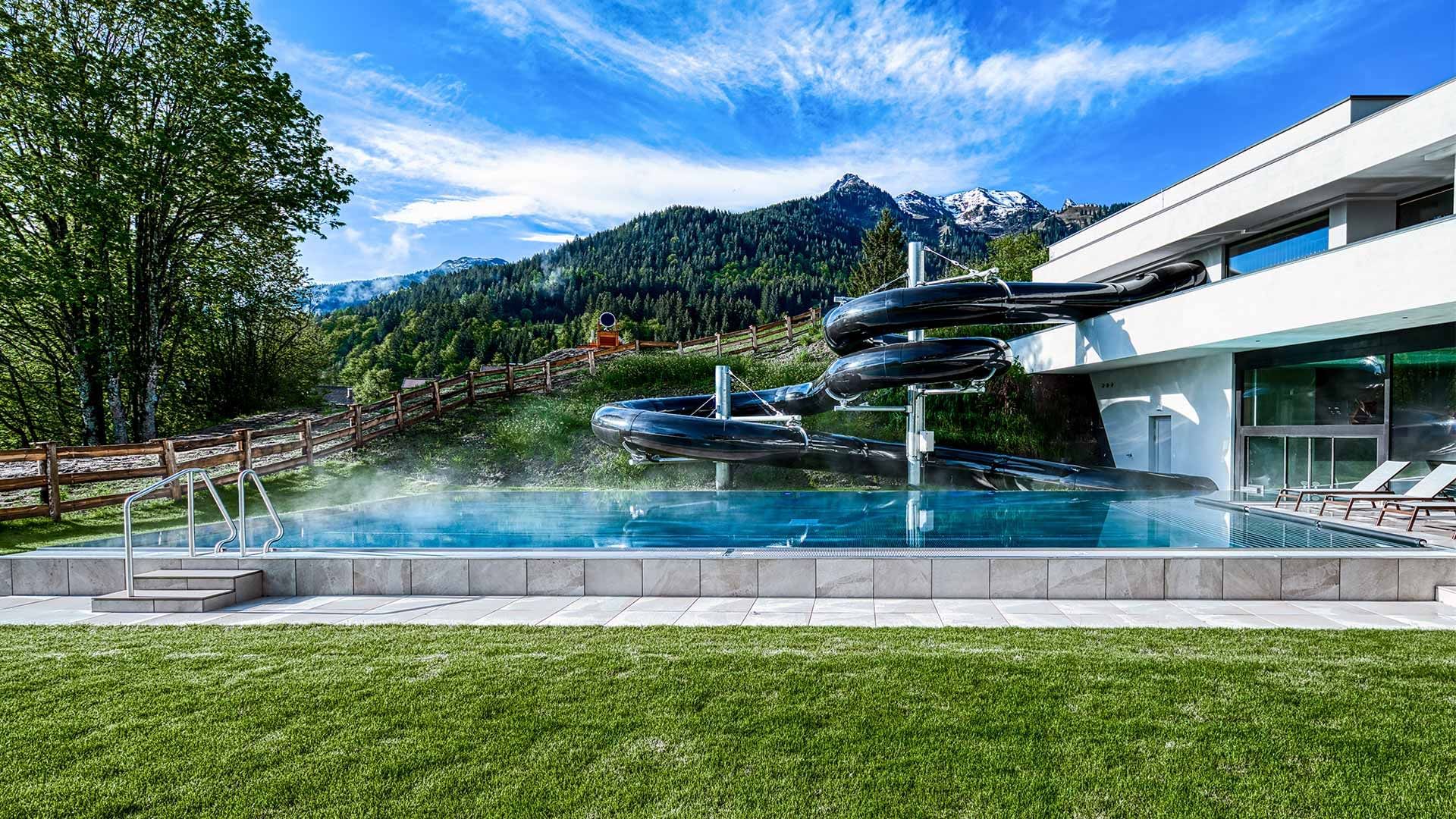 Falkensteiner Hotel Montafon exterior with waterslides in the pool with a mountain backdrop