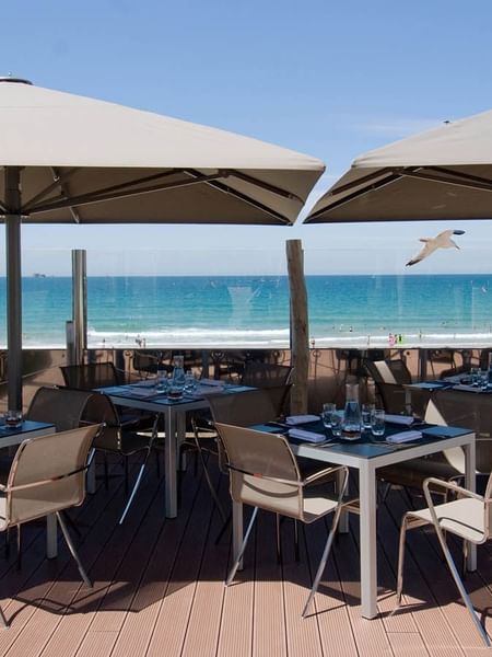 Modern outdoor tables and chairs positioned under large umbrellas in La Terrasse at Le Grand Hôtel des Thermes