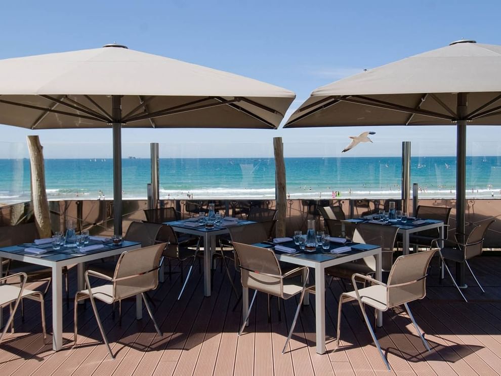 Modern outdoor tables and chairs positioned under large umbrellas in La Terrasse at Le Grand Hôtel des Thermes