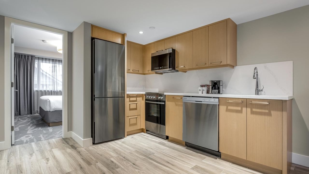 View of the full kitchen with oven, microwave, fridge, dishwasher and sink, with a view into the second bedroom
