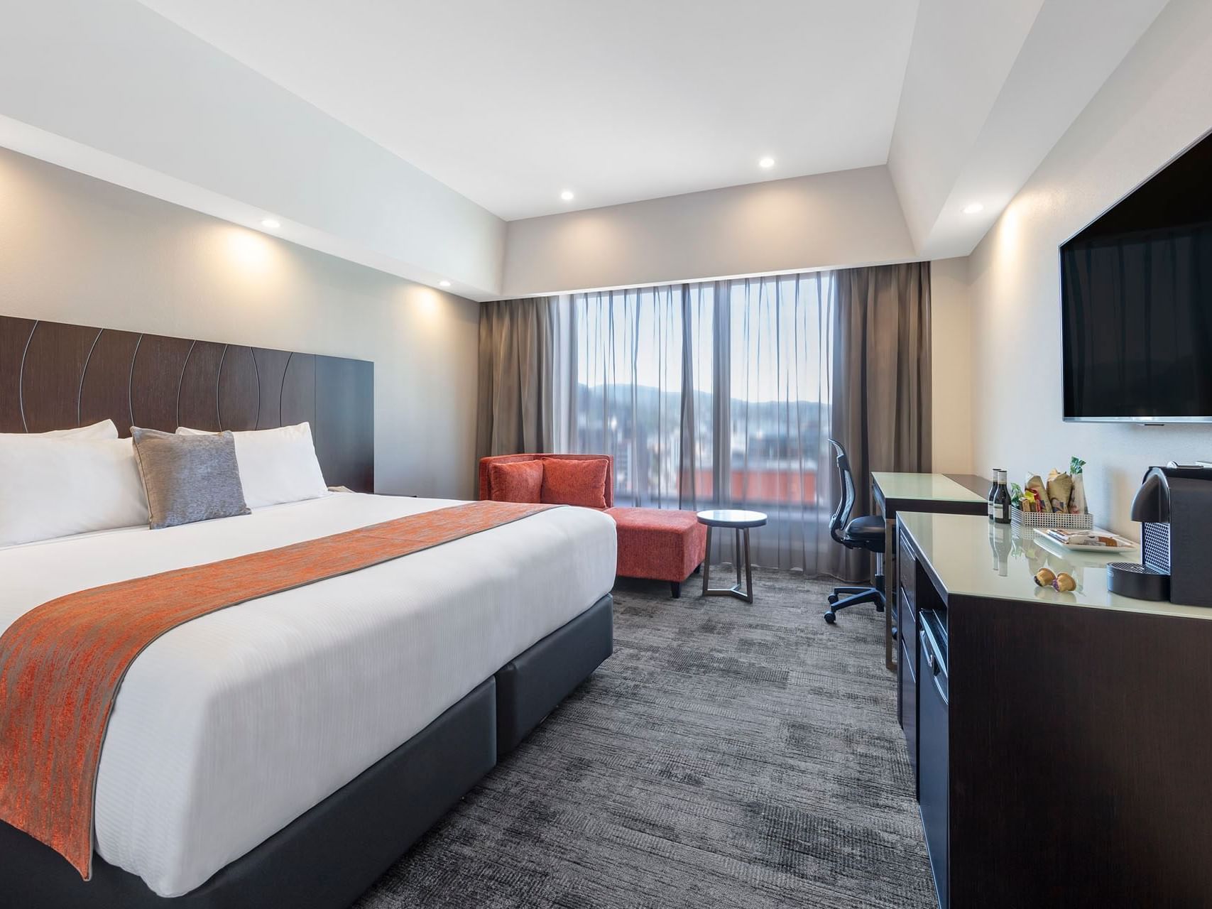 King bed, desk & sofa in a room with a city view at James Cook Grand Chancellor