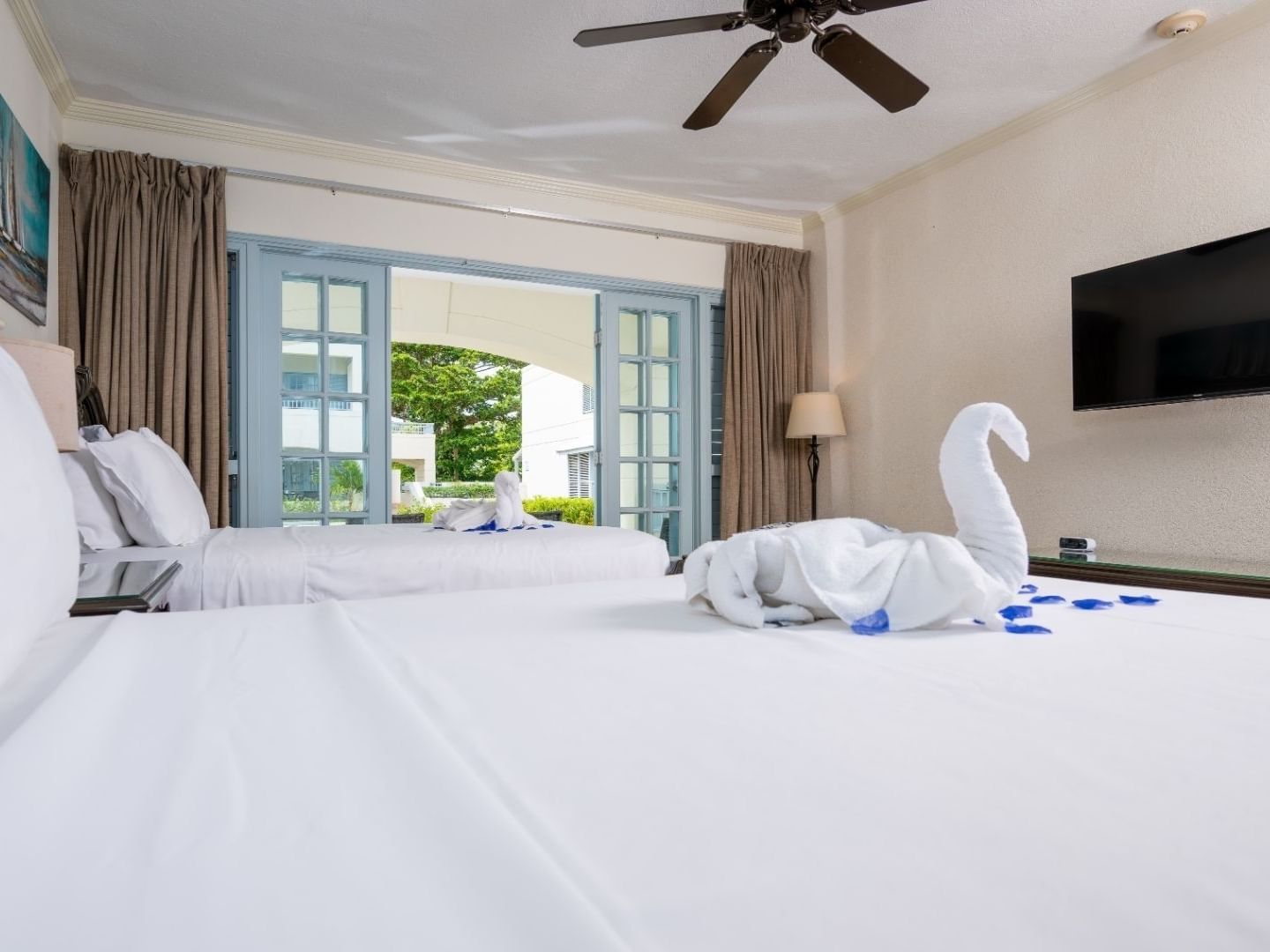 Two beds with white linens and a swan towel arrangement in a hotel room.