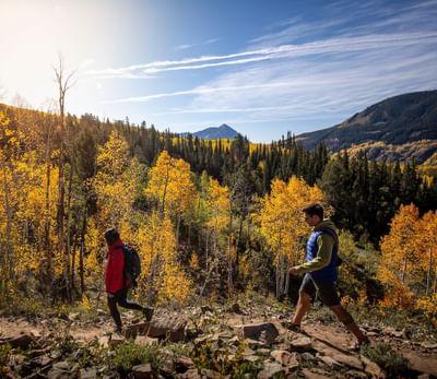 Two hikers walking on rocky path surrounded by fall foliage and mountains at Elevation Resort Spa