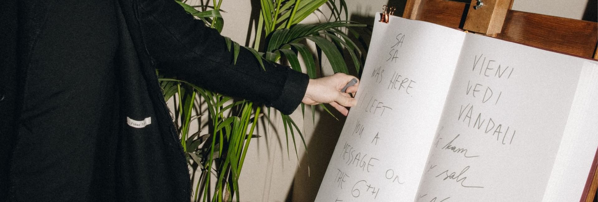 Hand pointing at a large open book with handwritten text on an easel at Hotel Motto Vienna