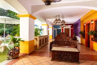 Vestíbulo colorido con arcos blancos, muebles tallados de madera y lámparas colgantes en Los Arcos Suites