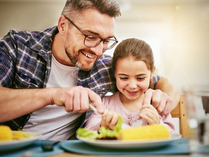 A happy father cutting his daughter's plated food in the restaurant at Hotel Topeka at City Center.
