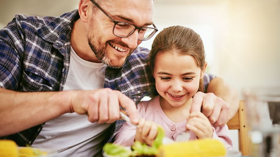 A happy father cutting his daughter's plated food in the restaurant at Hotel Topeka at City Center.