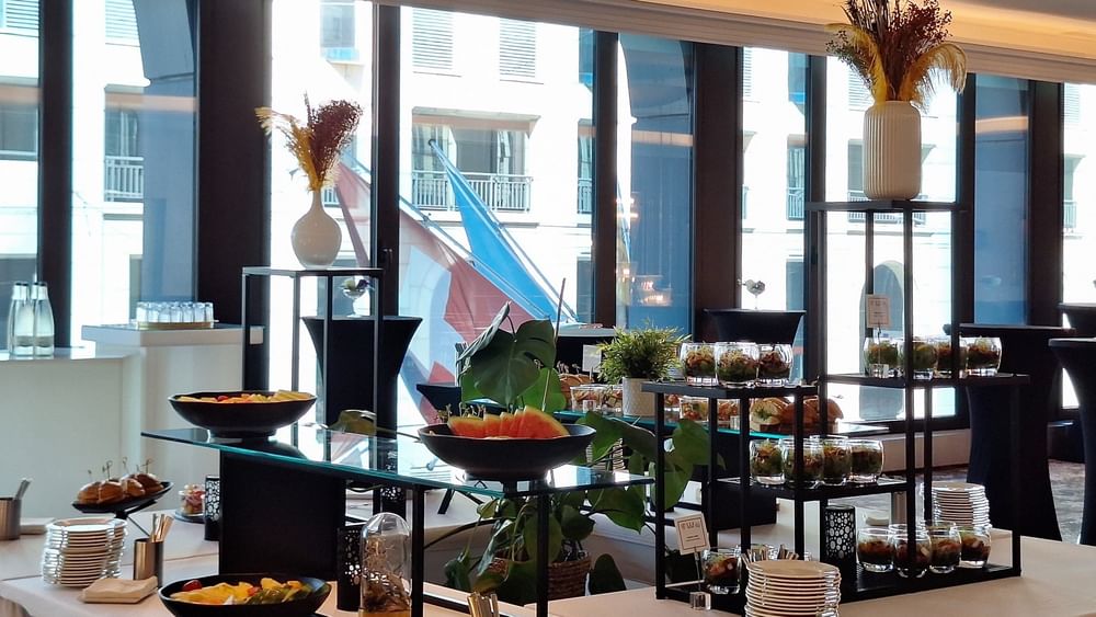 Bowls of fresh fruit and snacks on a white cloth table under bright windows in Foyer Mezzanine at Warwick Geneva