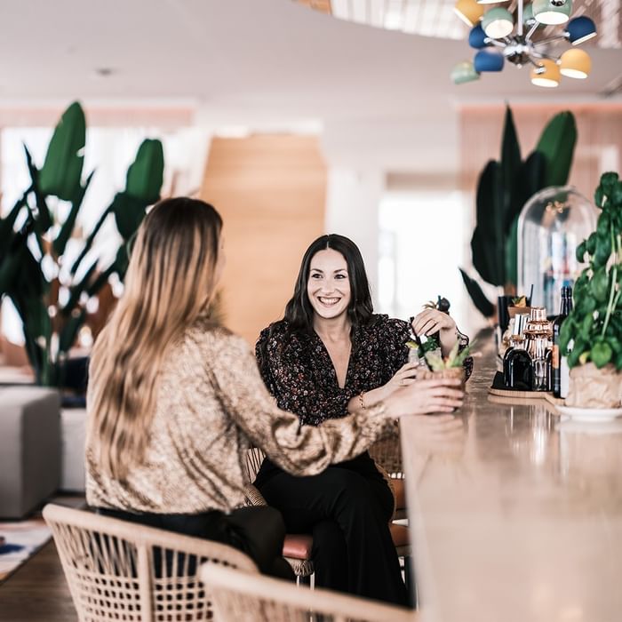 Due donne sorridenti conversano al bar presso Falkensteiner Hotel & Spa Jesolo