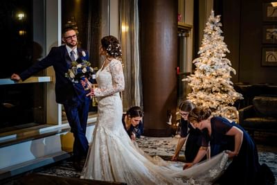 bridesmaids fixing brides dress next to white christmas tree
