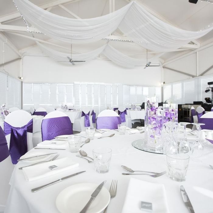 Elegant dining setup with white tables and chairs adorned with purple sashes at Mercure Hotel Townsville