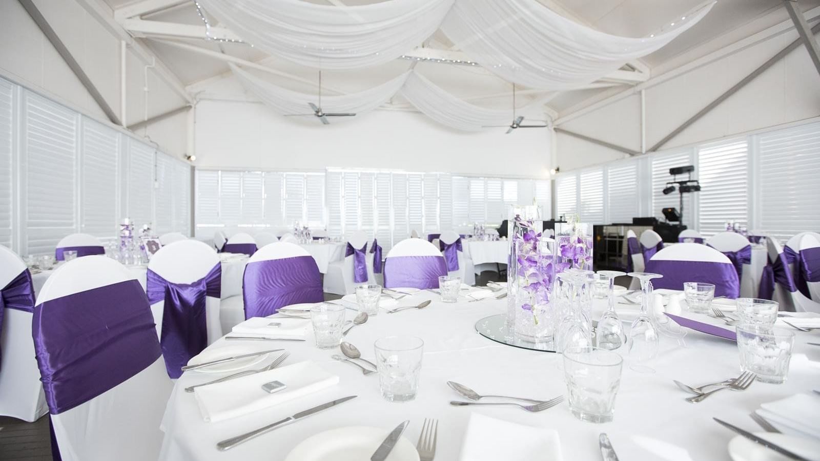 Elegant dining setup with white tables and chairs adorned with purple sashes at Mercure Hotel Townsville