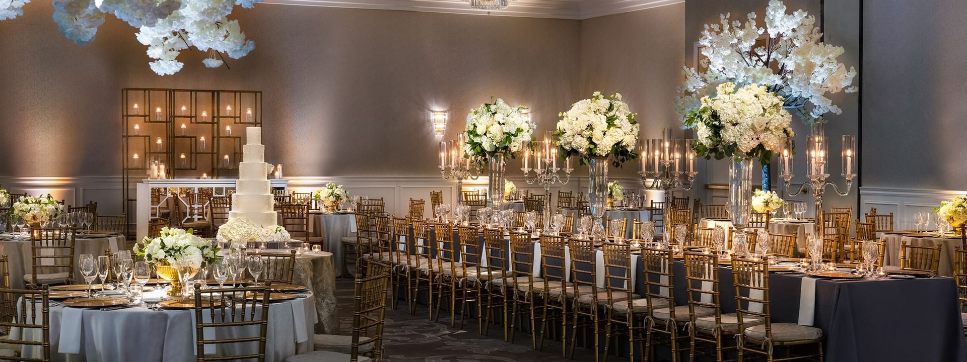 Long banquet tables by gold chairs under white floral towers in Turtle Creek Ballroom at Warwick Melrose Dallas