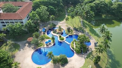 Aerial view of The Saujana Hotel Kuala Lumpur pool with sun loungers, palms, lush greenery, and a pond nearby