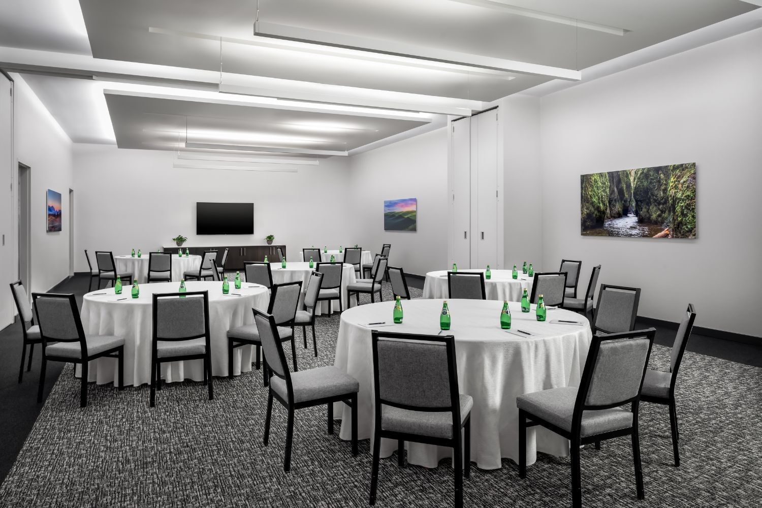Round dining tables with tablecloths and chairs set up facing the TV screen inside a spacious event room at Hotel X Toronto
