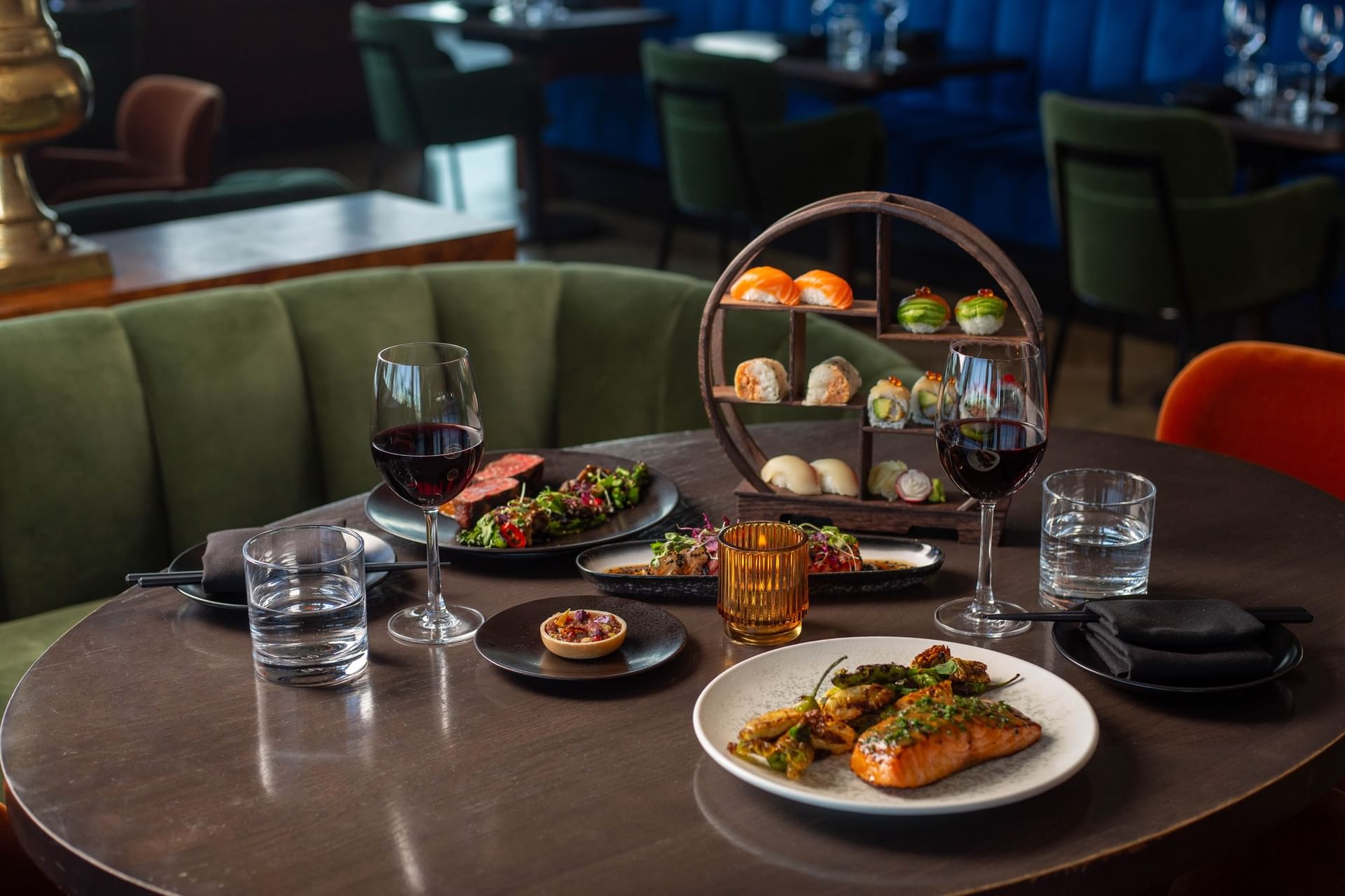 Two glasses of red wine and dishes like grilled salmon and seared beef are set on a table in Valerie at Hotel X Toronto