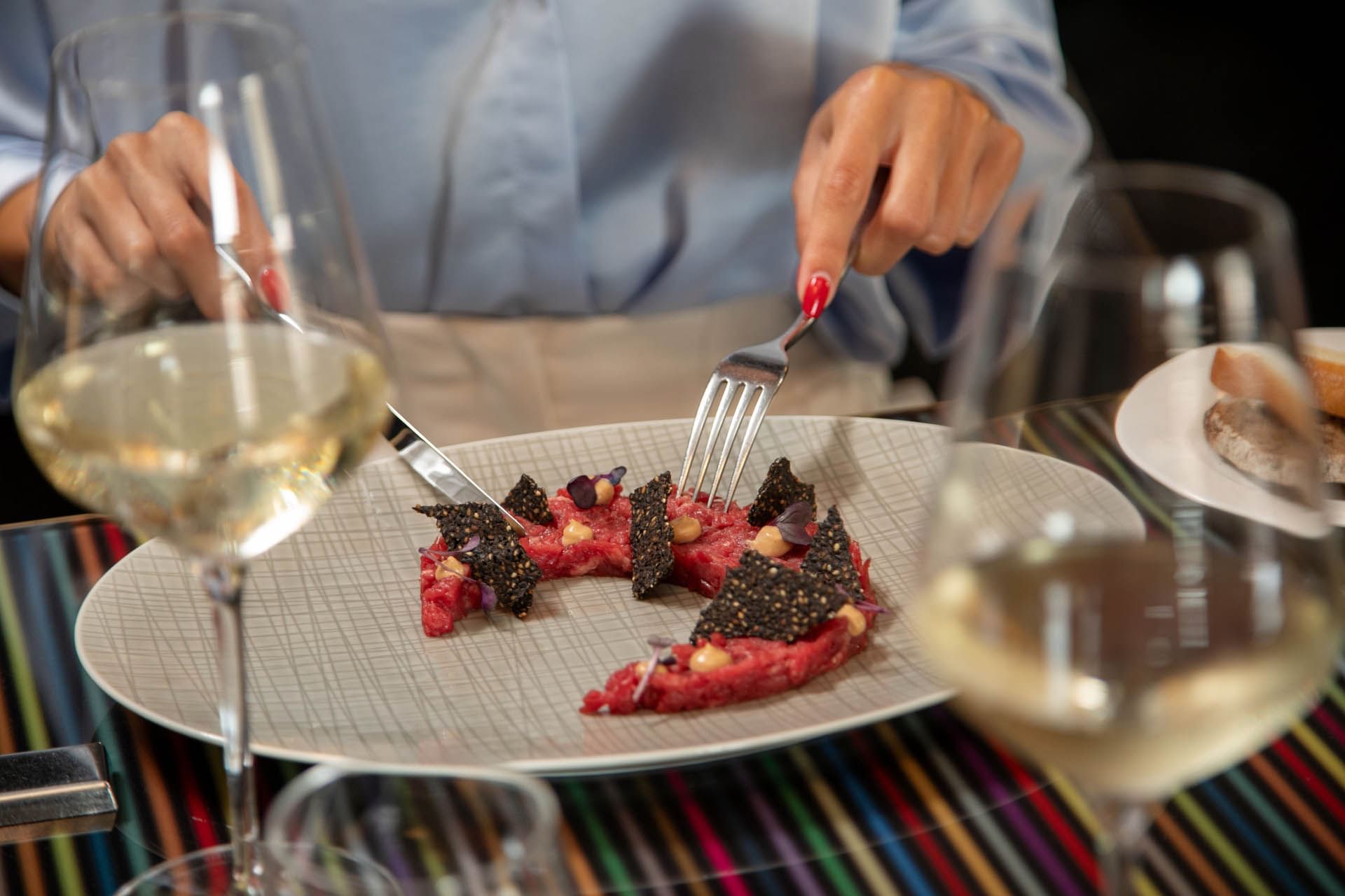 Cose-up of a person cutting into a gourmet dish of beef tartare garnished with black sesame served at The Glam Hotel