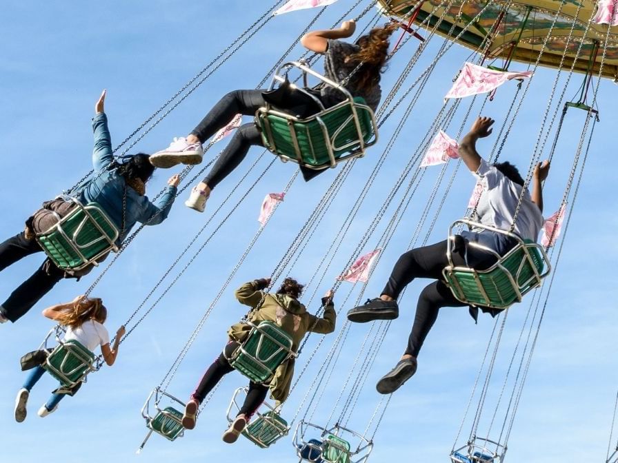 People enjoying a high-flying swing ride at a fair set against a blue sky near Camino Real Guadalajara