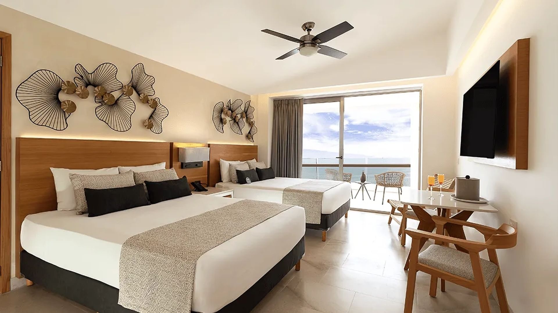 Habitación con una cama grande; almohadones decorativos; un sofá; un ventanal con vista al mar; respaldar de madera y mesa en el Sunset Plaza Beach Resort, uno de los mejores hoteles con todo incluido en México