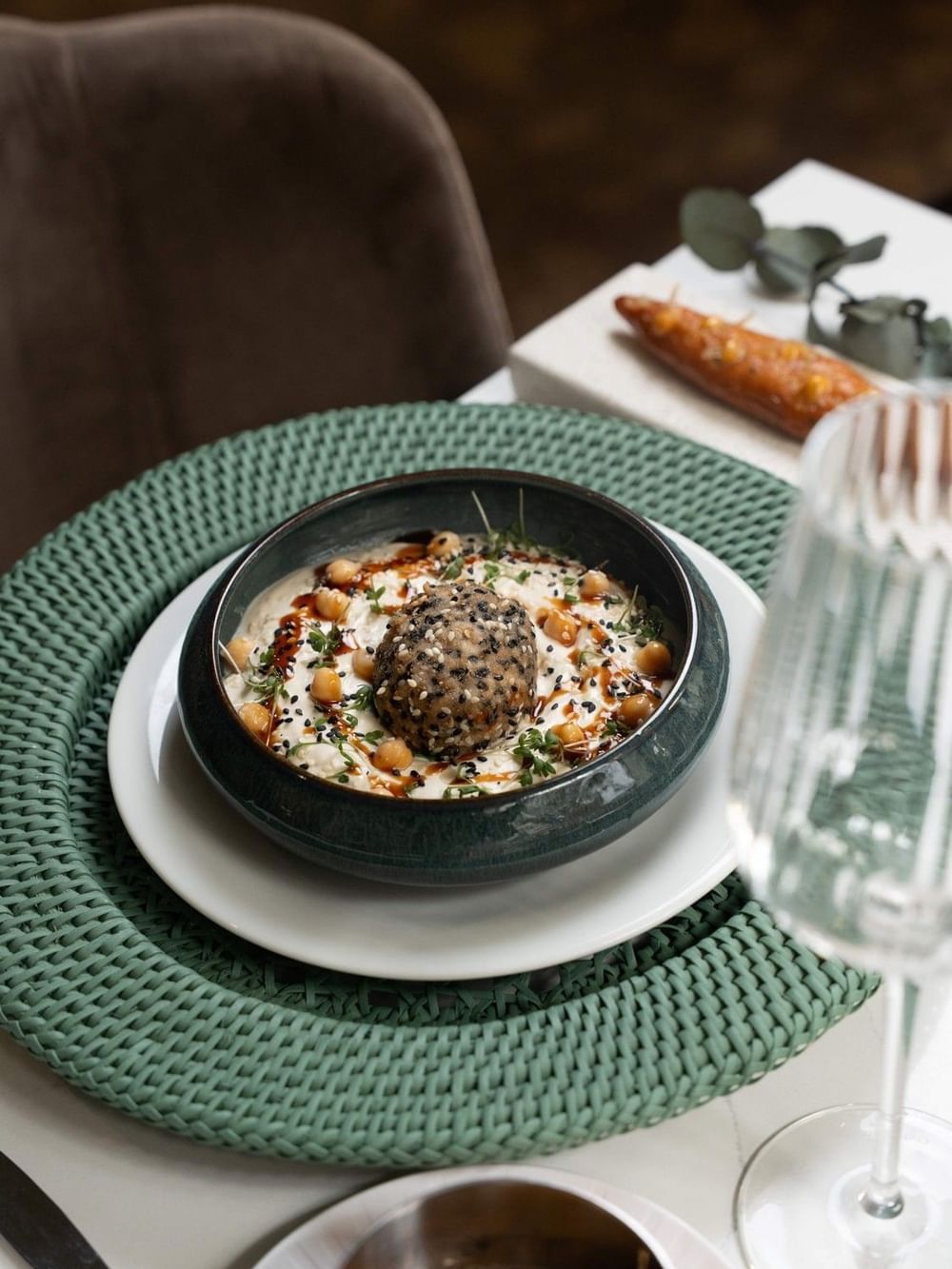 Round bowl of hummus with chickpeas and black seeds, served on a green placemat, served at Hotel Westminster Paris