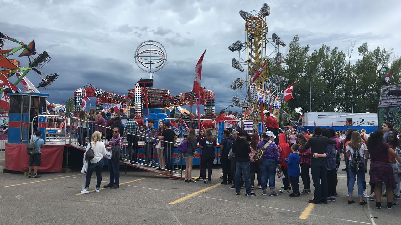 Crowds gather around colorful carnival rides and attractions under a cloudy sky at the Calgary Stampede.