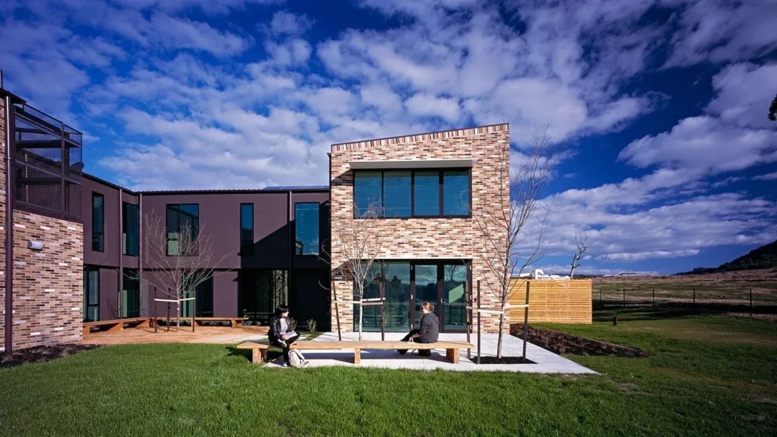 Modern brick building with two people sitting on a bench at La Trobe University - McFarlane's Hill Residences.