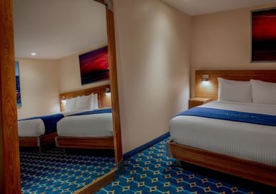 Two beds beside a floor mirror reflecting a wall art piece in Double Queen Cabin with no windows at Harborside Inn Boston