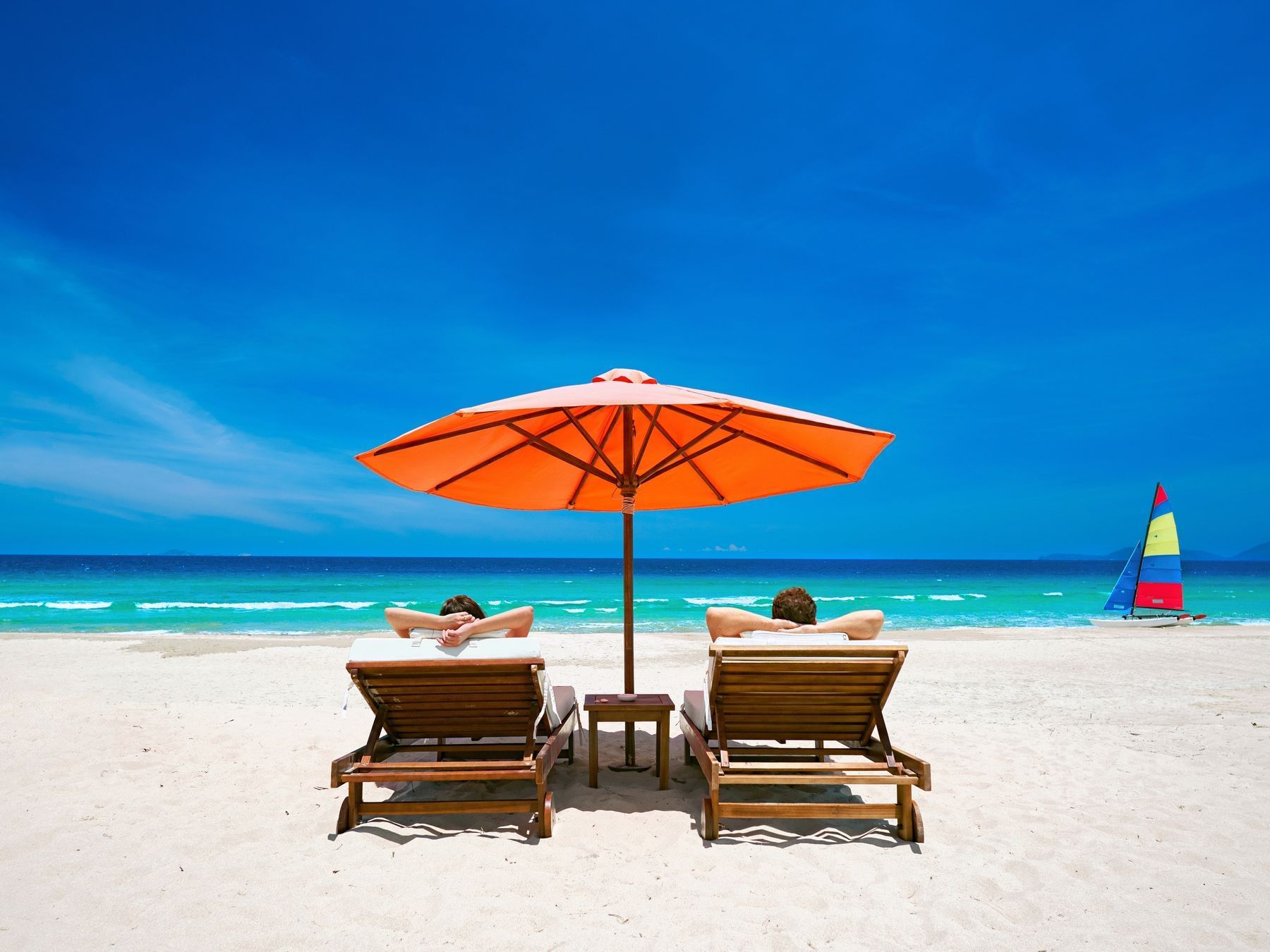 couple lounging under orange umbrella on beach with bright blue skies