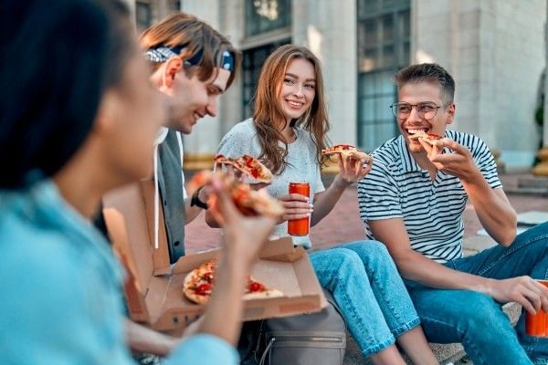 Four smiling college students sit and eat slices of pizza.