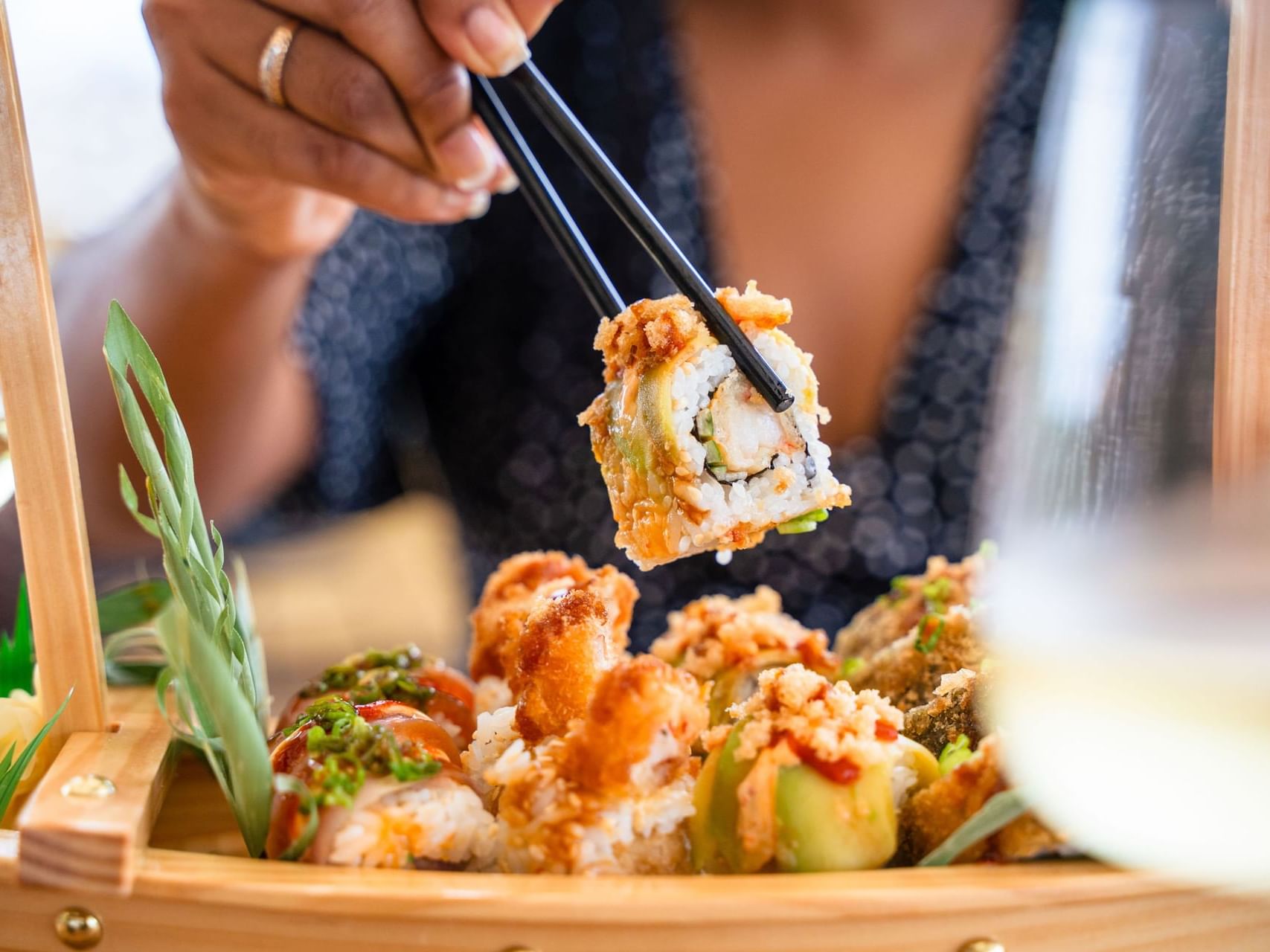 Close-up van een hand die met stokjes een stuk sushi oppakt geserveerd in Bobbie’s Beach Club bij Golden Rock Resort