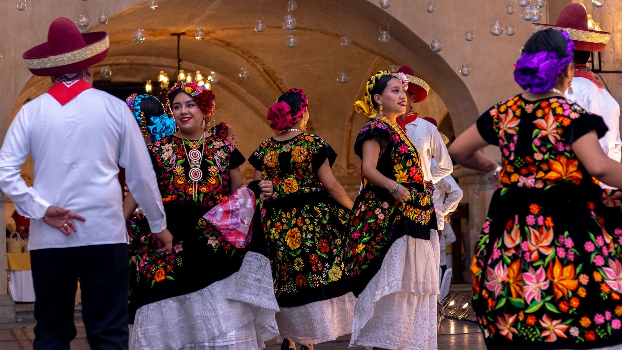 Dancers in vibrant floral dresses performing in a grand historic ballroom at Quinta Real Oaxaca