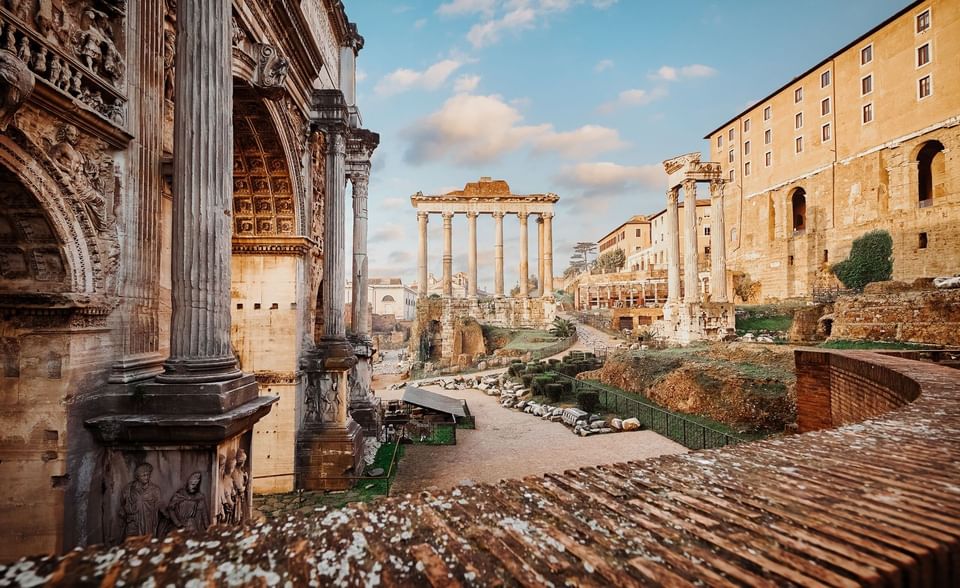 Ancient ruins of the Roman Forum and Arch of Septimius Severus under soft blue clouds and sunlight near Meraviglia