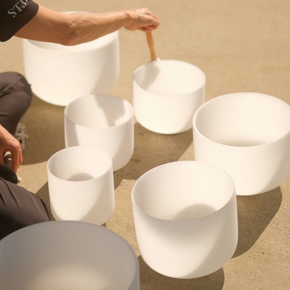 A person is playing a set of white crystal singing bowls with a mallet.