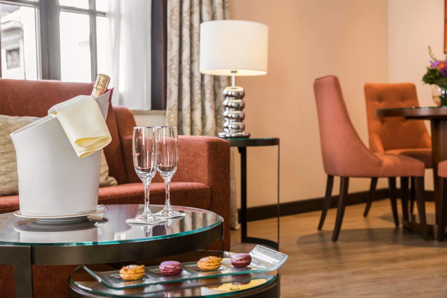Bucket with champagne & glasses by macarons on a glass table in Junior Suite Privilege View at Warwick Grand Place Brussels
