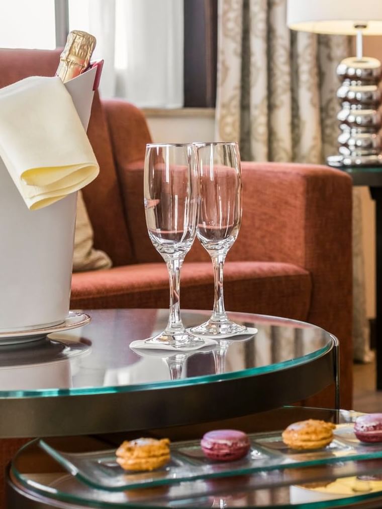 Bucket with champagne & glasses by macarons on a glass table in Junior Suite Privilege View at Warwick Grand Place Brussels