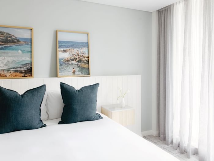 Village Balcony Queen at Elysium Manly with dark teal pillows on a bed by a small nightstand under coastal scenery wall art