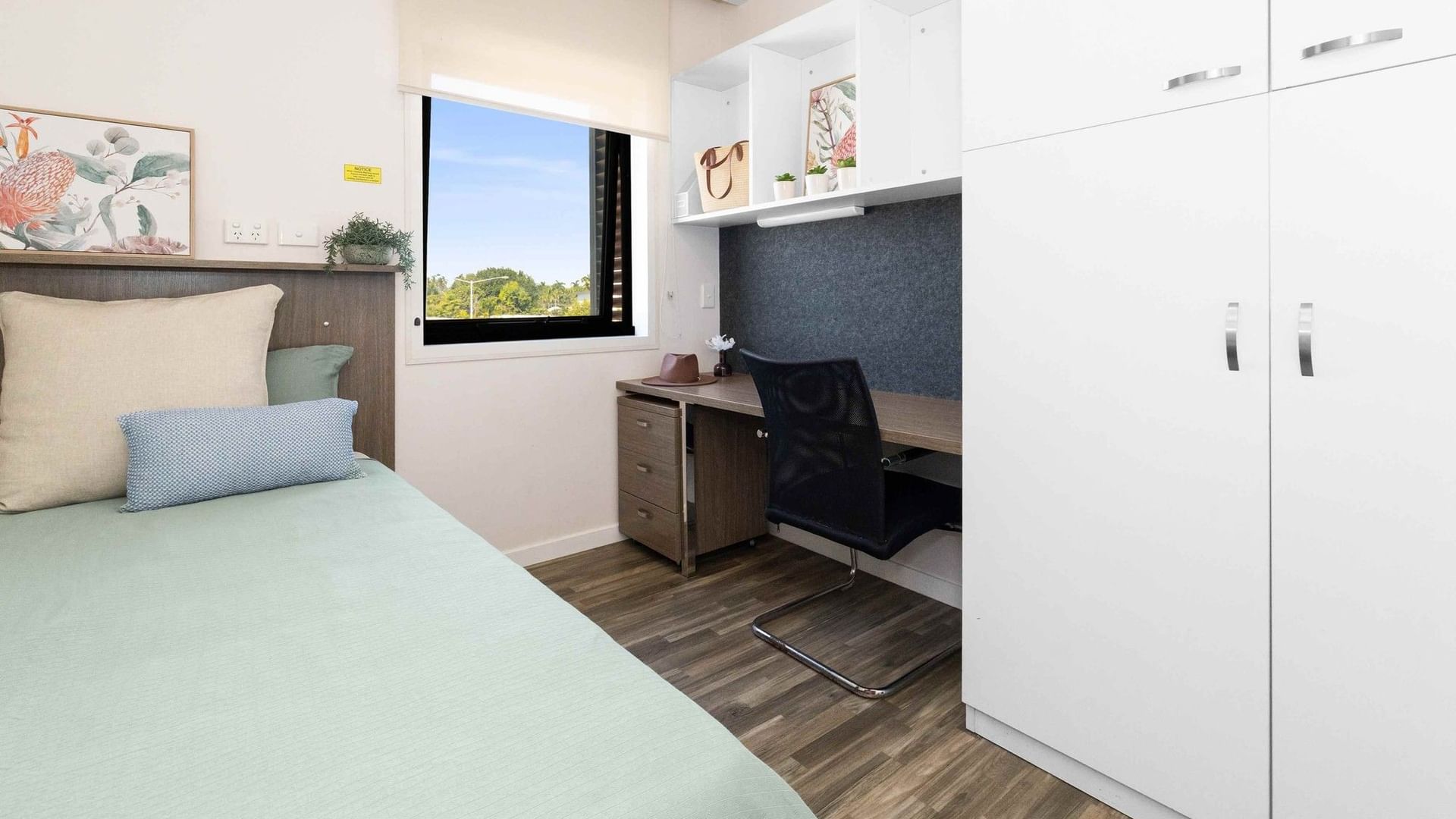 A cozy bedroom with bed, desk, chair, and window at UniLodge Darwin.