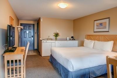 Bed placed next to the kitchenette with a desk and TV positioned by the door in room at Hilltop Inn Salmon Arm