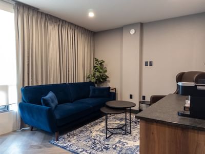 A modern hotel room with blue couch, coffee tables, and a bar area at Carriage House Hotel Conference Centre