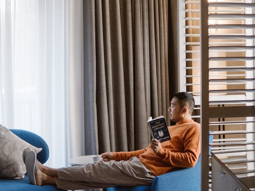Man relaxing with a book in a hotel room for Weekend Getaway Offer.