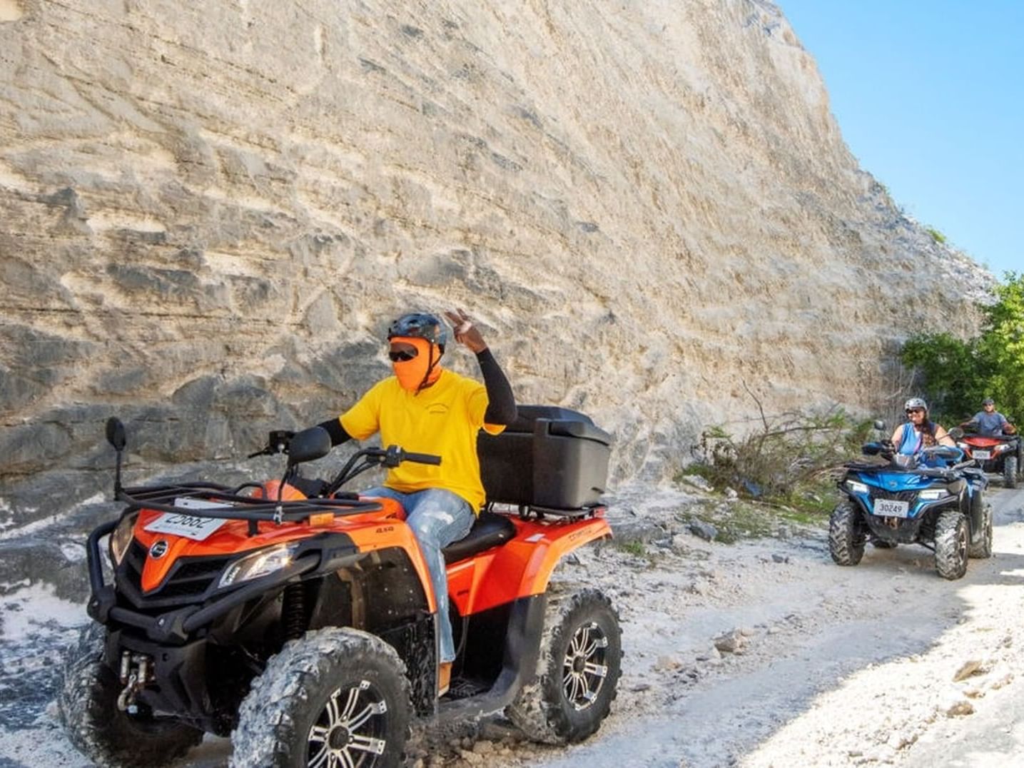 Two ATV riders navigate a sandy path alongside a steep near Windsong Resort On The Reef