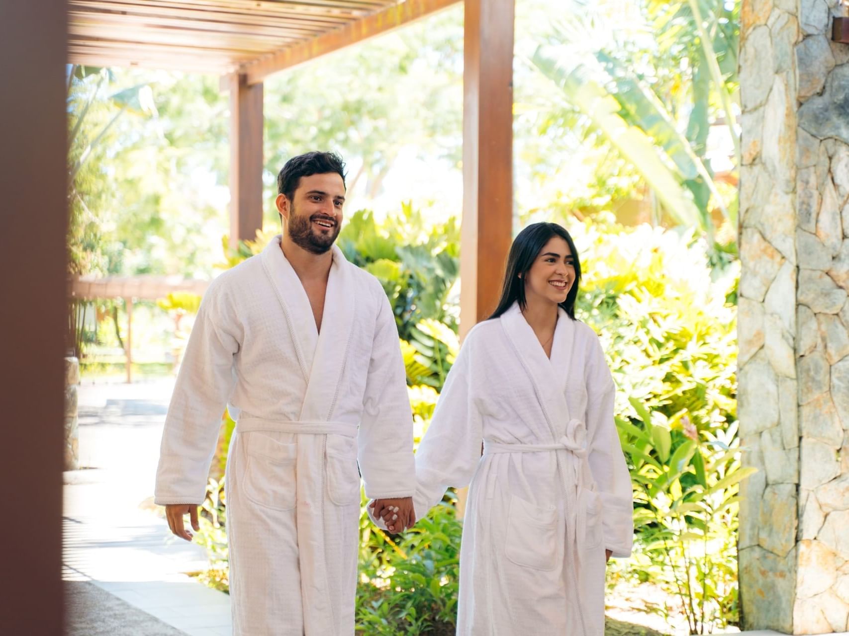 Couple in robes holding hands & walking in the Maina Spa at Indura Beach & Golf Resort