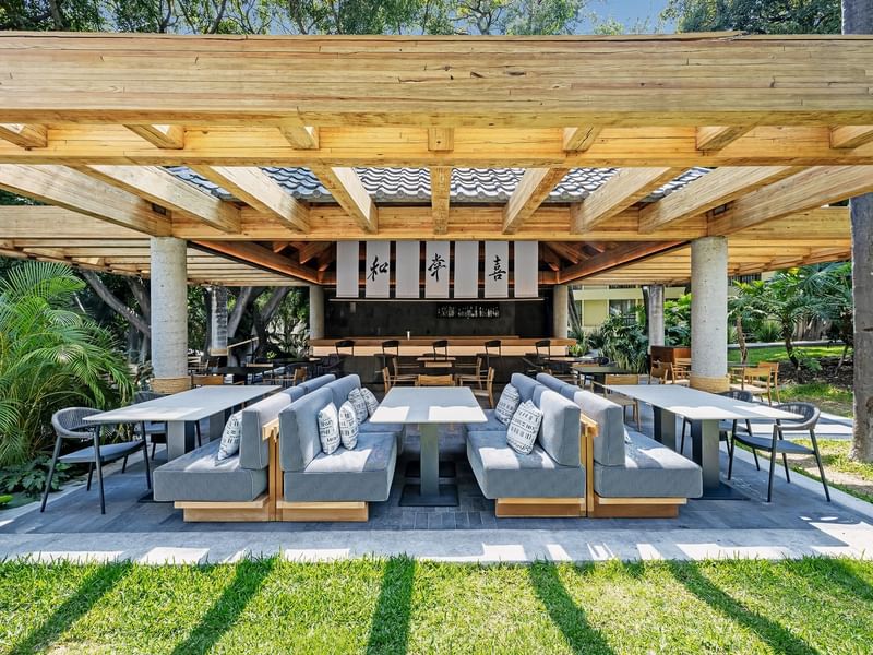 Outdoor dining area with wooden pergola, booths, and cushions, surrounded by lush greenery at Grand Fiesta Americana
