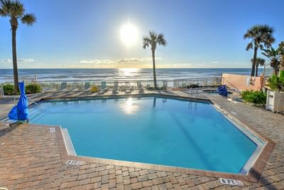 Outdoor pool at the Daytona Bahama House Boutique Hotel with beach chairs, palm trees, and ocean view at sunset.