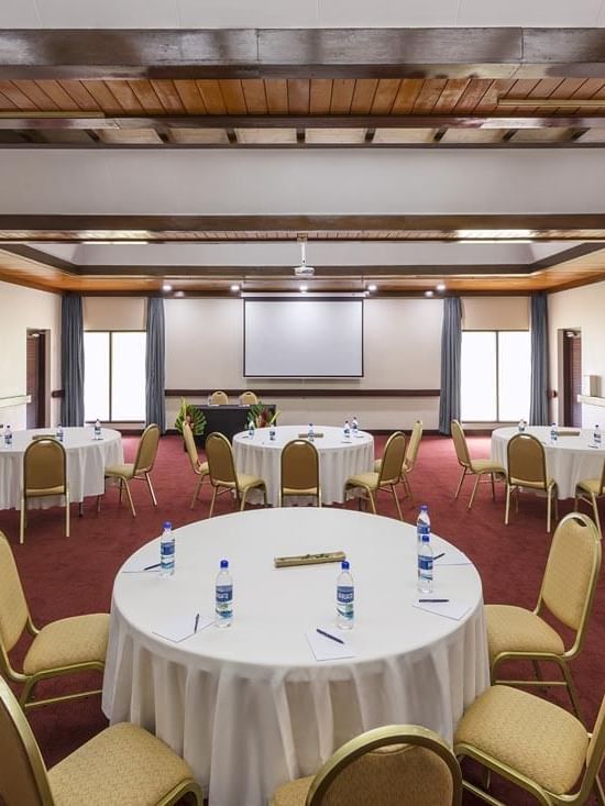 Spacious meeting room with round banquet tables and a projector screen at Warwick Le Lagon