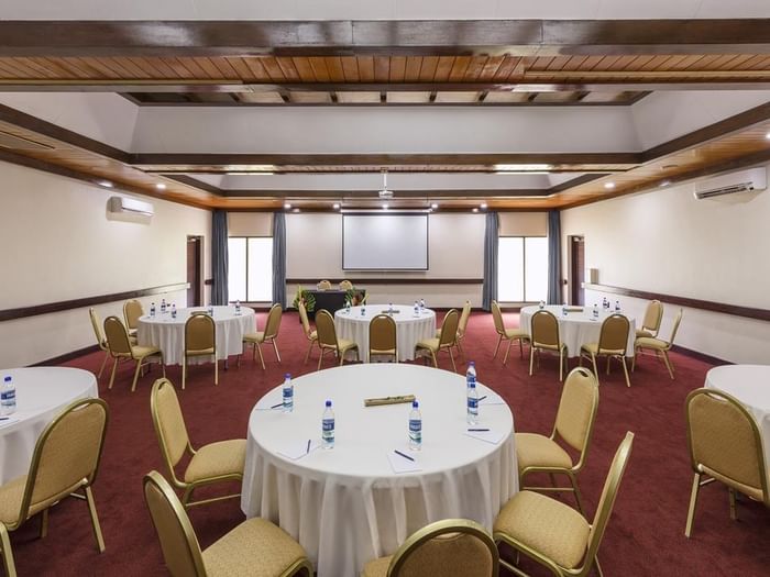 Spacious meeting room with round banquet tables and a projector screen at Warwick Le Lagon