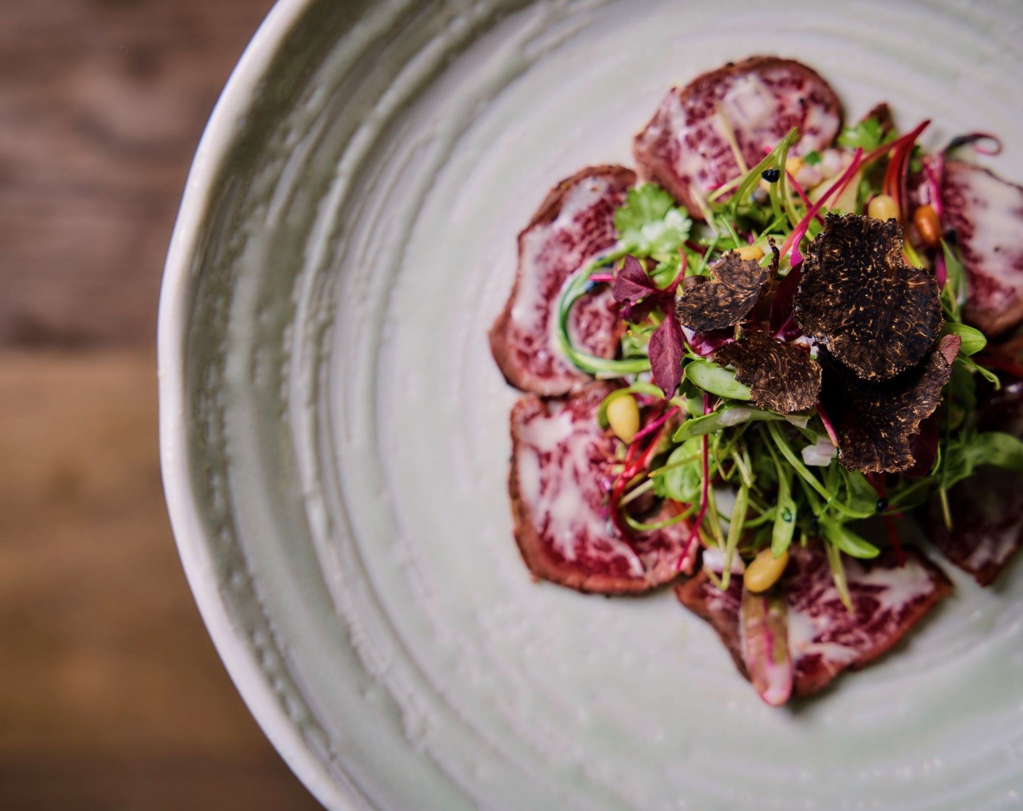 A plate of thinly sliced beef with green vegetables and black truffle toppings