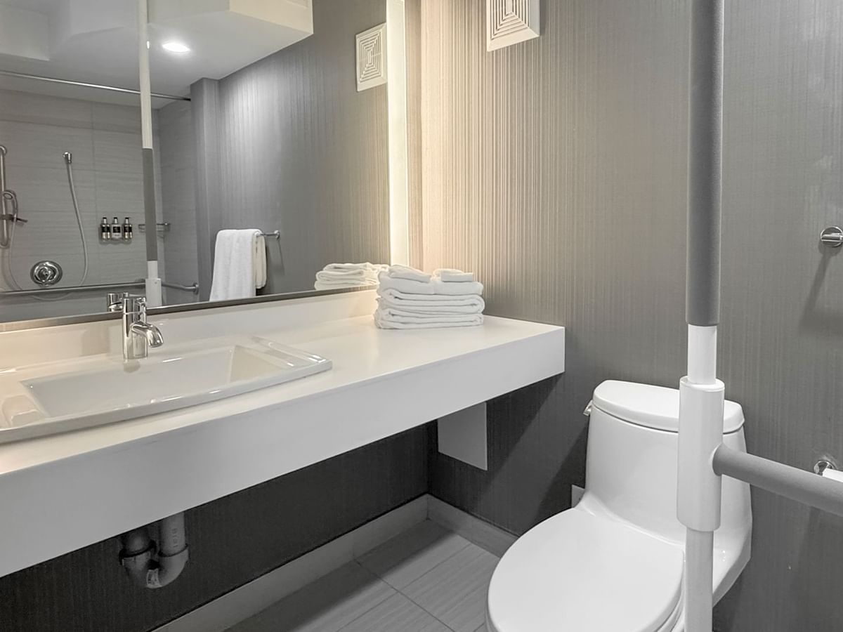 Accessible bathroom with a toilet, sink, mirror, white towels, and grab bars.